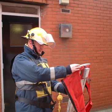 Andy Graham, founder of MHFA Training UK as a firefighter in gear handling equipment near brick building.