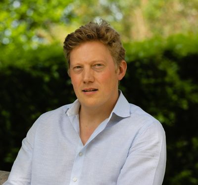 Man in white shirt outdoors with greenery background.
