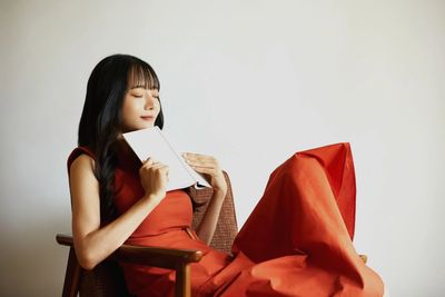 Woman in red dress peacefully holding a book with eyes closed.