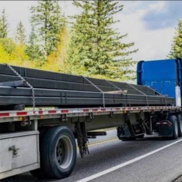 Flatbed truck carrying long metal beams on a highway.