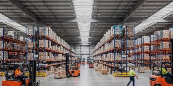 Busy warehouse with forklifts and stocked shelves under bright lighting.