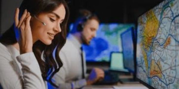 Two people monitoring maps on computer screens with headsets.