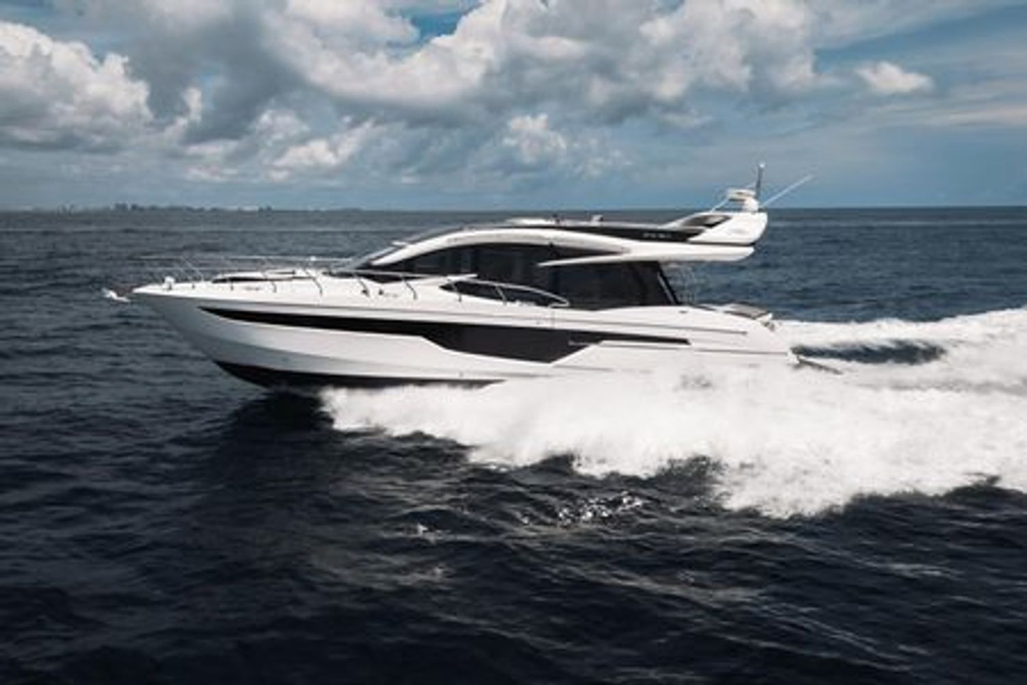 A sleek white yacht speeding across the ocean under a cloudy sky.