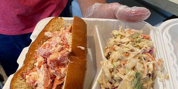Lobster roll and coleslaw in a takeout container.