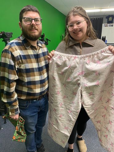 Two people holding and displaying a pair of large pajama pants indoors.