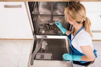 Woman cleaning a dishwasher with gloves in a kitchen.