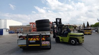 A forklift loads large tires onto a flatbed truck in an industrial area.