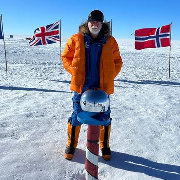 Man in orange jacket standing on snowy ground with British and Norwegian flags.