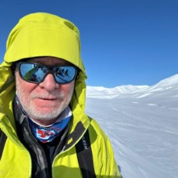 Man in bright yellow jacket and sunglasses in snowy mountains.