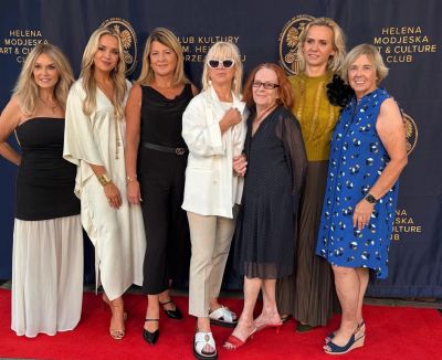 Group of seven women posing on a red carpet.