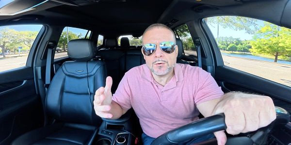 Man in sunglasses talking while driving a car.