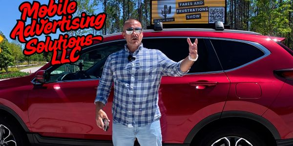 Man in checkered shirt stands by red SUV advertising mobile advertising solutions.
