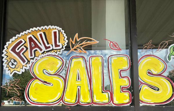 Brightly painted window sign advertising a fall sale with autumn leaves.