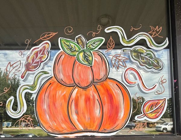 Colorful autumn-themed window painting with pumpkins and swirling leaves.