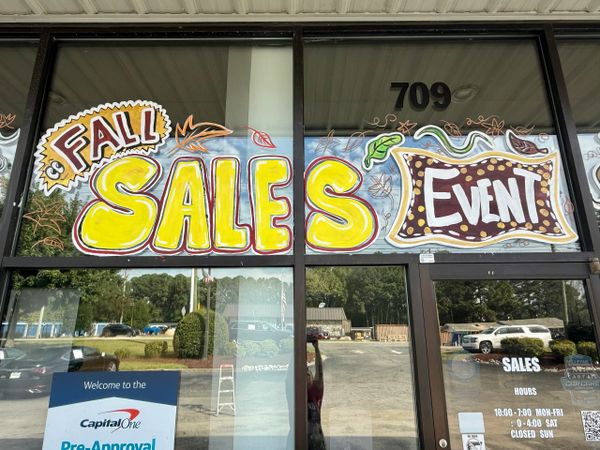 Brightly painted window sign advertising a fall sales event at a store.