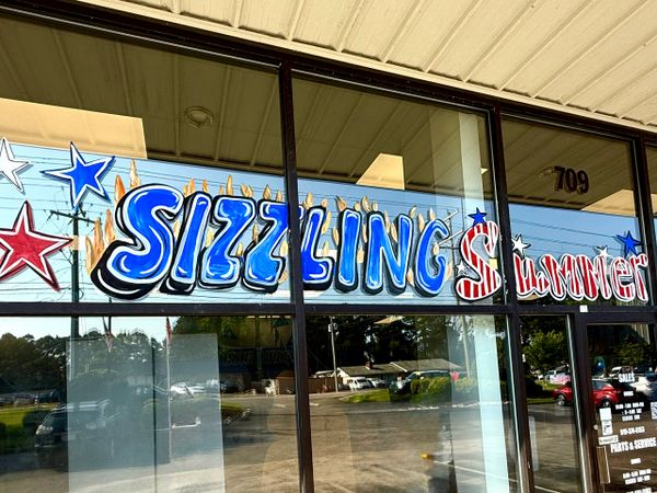Colorful window painting with "Sizzling Summer" and stars at storefront.