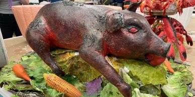 A roasted pig on leafy greens with vegetables.