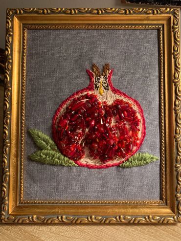 Framed embroidery of a pomegranate with detailed seeds and leaves.