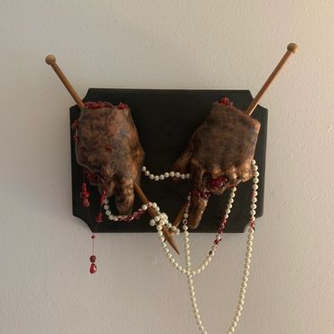 Creepy hands with knitting needles and pearls on a black plaque.