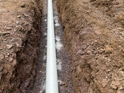 A white pipe laid in a trench filled with gravel.