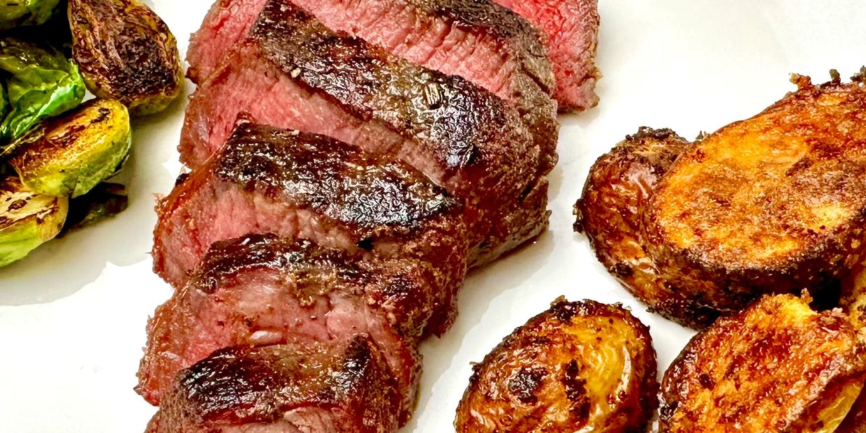 Elk Medallions sliced on a plate with brussels sprouts and air fried potatoes.