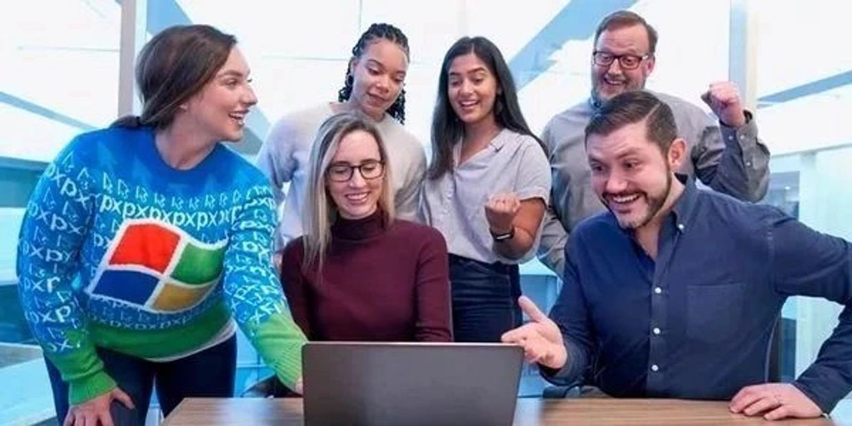 A group of colleagues excitedly looking at a laptop in an office.