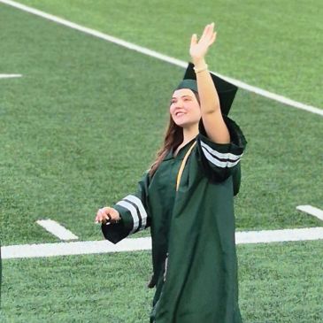 Graduate in cap and gown waving on a field.
