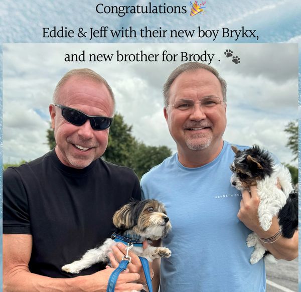 Two men smiling, each holding a small dog, celebrating a new puppy addition.