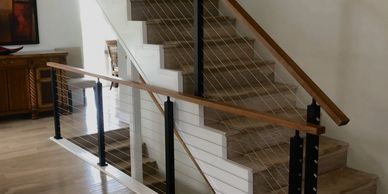 Modern indoor staircase with wooden handrails and metal cable balusters.