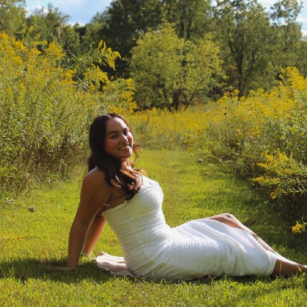 Woman in white dress sitting on grass surrounded by yellow flowers.