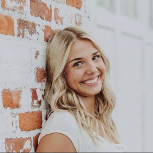 Smiling young woman leaning against a brick wall.