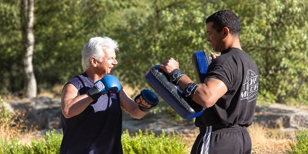 Senior woman boxing with coach outdoors.