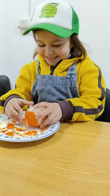 Niña pelando una mandarina con sonrisa.
