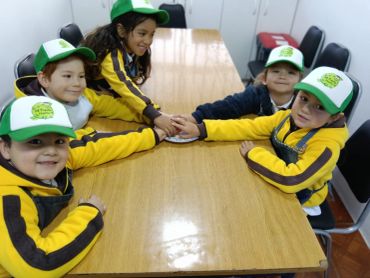 Niños con gorras verdes y amarillas, unidos en una mesa.