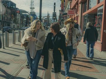 Three women walking and chatting on a city street.