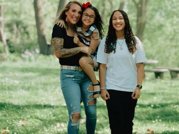 A woman with two girls smiling outdoors.