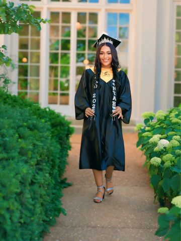 Graduate in cap and gown walking on pathway.