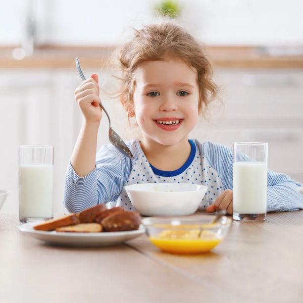A photo of a young girl eating breakfast cereal with a glass of milk.