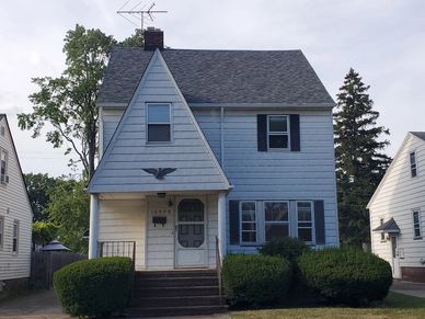 Two-story blue house with bushy green shrubs.