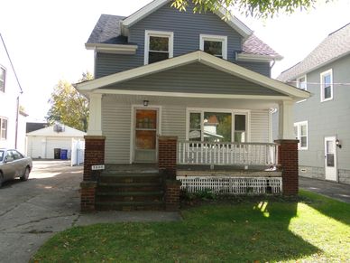 A two-story gray house with a front porch and brick pillars.