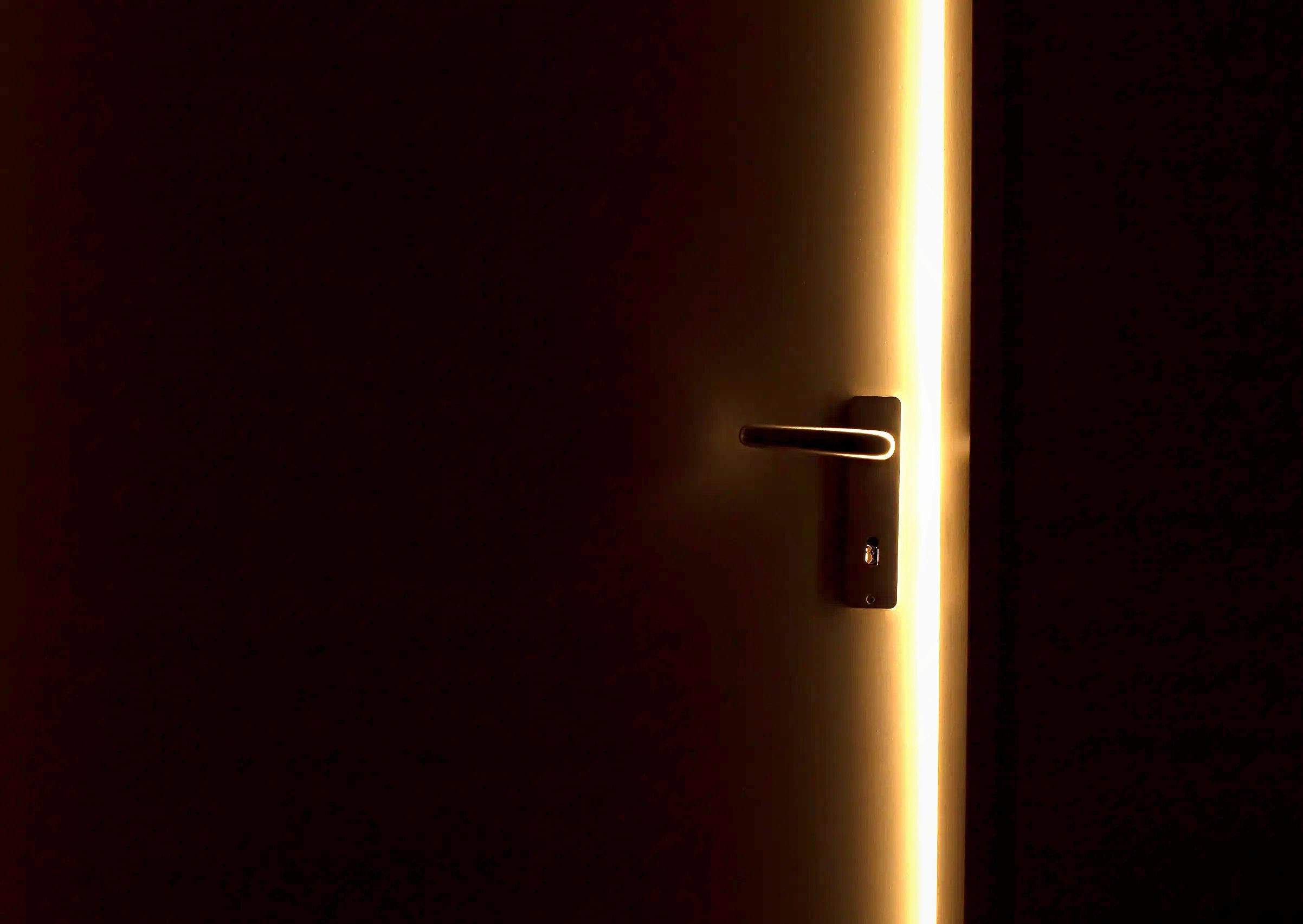Lit slit of door opening with door handle and black foreground