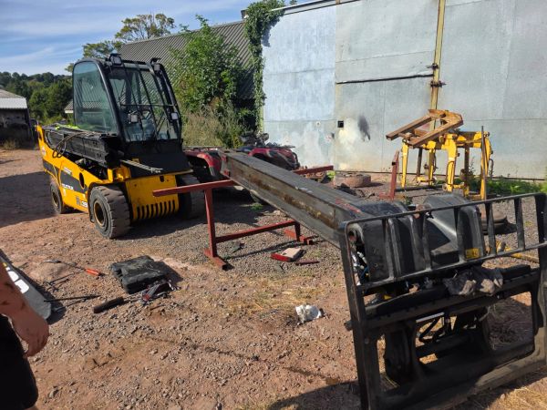 Yellow forklift with extended arm in outdoor yard.