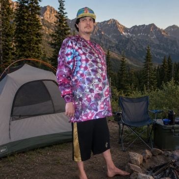 Man in colorful shirt camping barefoot with mountains in the background.