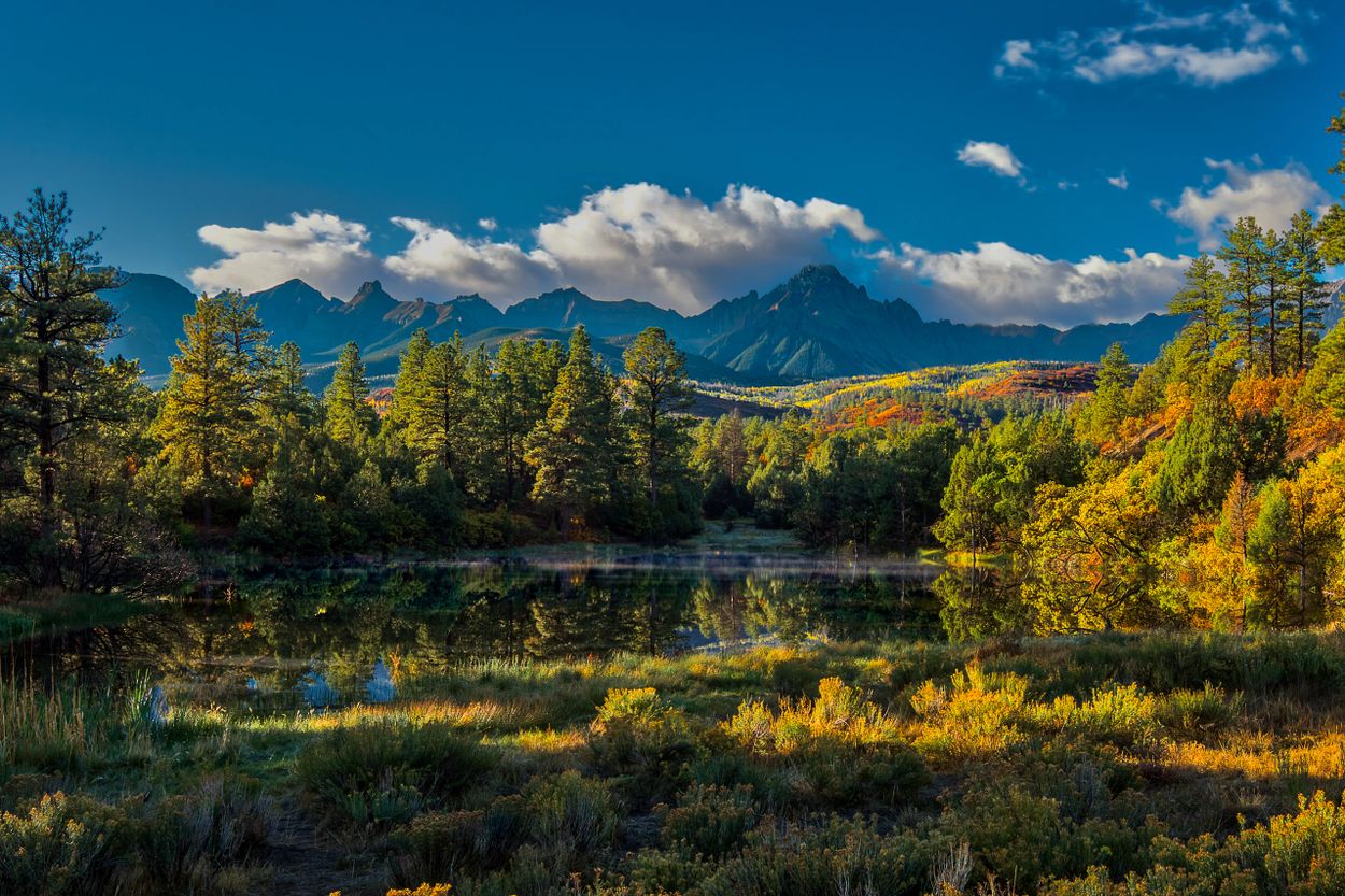 Serene lake surrounded by autumn trees with mountains in the background.