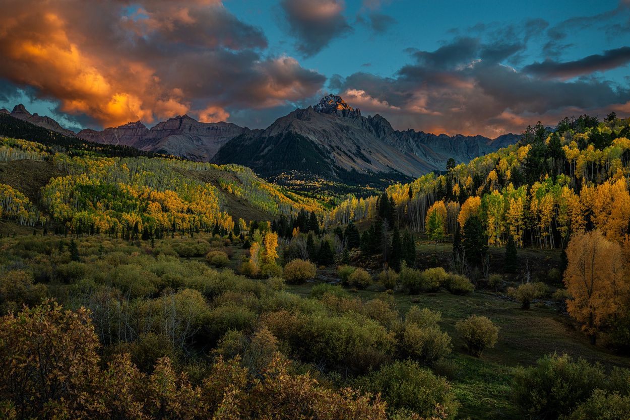 Sunset over a colorful autumn mountain landscape with dramatic clouds.
