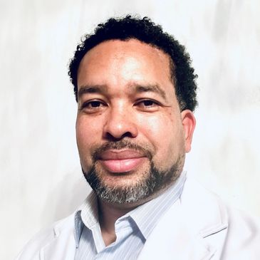 Portrait of a man with curly hair and a beard wearing a white coat.