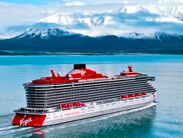 Virgin Voyages cruise ship sailing near snowy mountains.