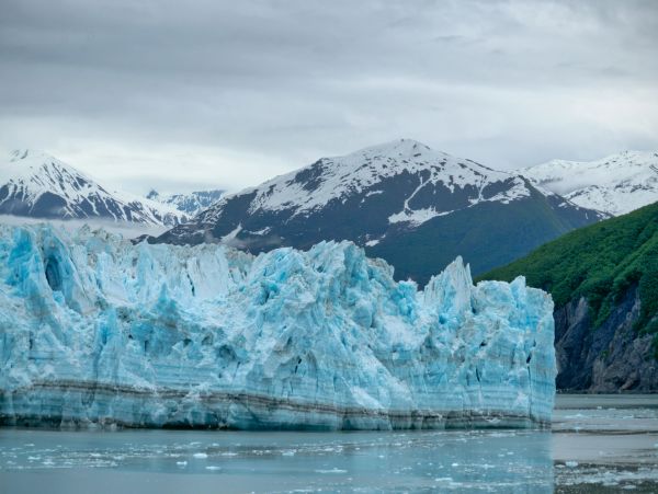 Blue glacier surrounded by snowy mountains and green forests.