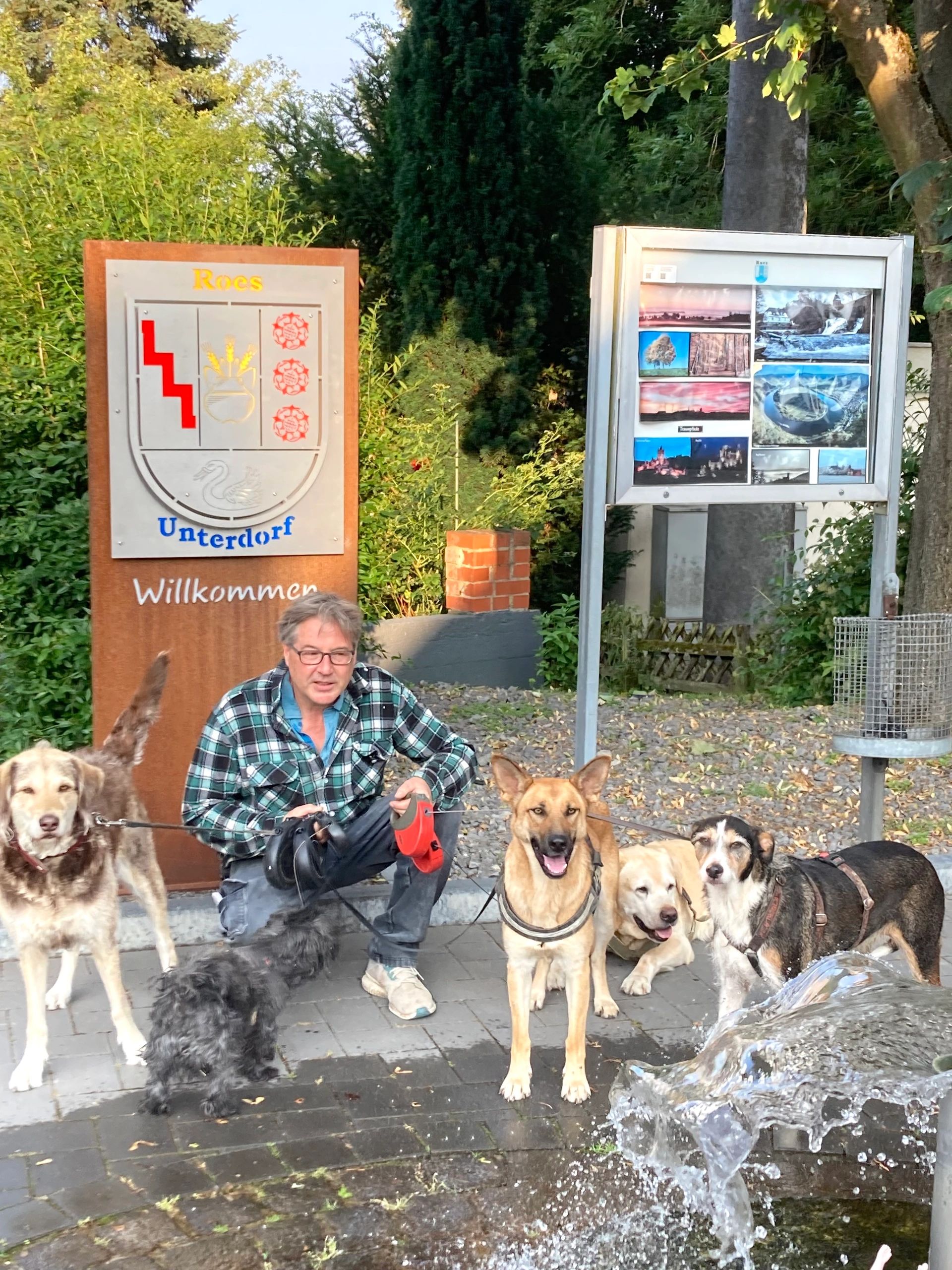Mann mit 5 Hunden vor dem Dorfbrunnen
