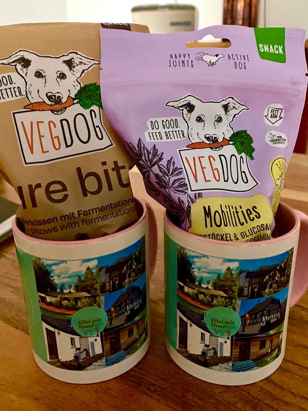 Two mugs holding bags of VegDog dog snacks with colorful packaging.
